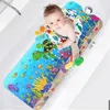 A baby is lying on a colorful bath mat in a bathtub. Produktbild-Vorschau