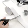 A hand is using scissors to cut a roll of white sealing tape next to a stove. Anteprima dell’immagine prodotto
