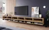 A modern living room with a TV mounted on the wall above a long, wooden TV stand. The TV stand has multiple compartments, some open and some closed, displaying books and decorative items. A floor lamp and a piece of abstract art are also visible. Voir les images du produit