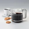 A coffee maker carafe filled with coffee, a coffee cup, and cookies on a white surface. Produktbild-Vorschau