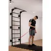 A man is exercising with a resistance band attached to a wall-mounted pull-up bar and ladder. Produktbild-Vorschau