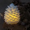 A lit pinecone decoration sits on a piece of bark, surrounded by other pinecones. Produktbild-Vorschau