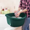 A person is washing clothes in a green basin in a bathroom. Podgląd zdjęcia produktu