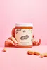 Hands holding a jar of peanut butter in front of a pink background. Produktbild-Vorschau