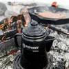 A black coffee pot sits on a grate over a campfire, with a cast iron skillet cooking food in the background. Produktbild-Vorschau