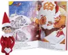 An Elf on the Shelf doll is placed next to an open children's book with illustrations of Santa and elves. Produktbild-Vorschau