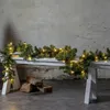 A garland with lights draped over a white bench, with logs on the ground. Produktbild-Vorschau