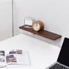 A shelf with a clock and a jar on it, above a desk with a book and a laptop. Produktbild-Vorschau