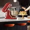 A person is decorating a cake with a piping bag, next to a red stand mixer with a stainless steel bowl. Produktbild-Vorschau