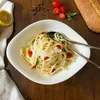 A bowl of pasta with cherry tomatoes and basil, served with a lemon wedge and a loaf of bread on a wooden table. Voir les images du produit