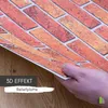A hand holding a 3D wall panel with a brick pattern over a wooden surface. Produktbild-Vorschau