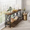 A console table with decorative metalwork is placed against a large window, with a lamp, fruit, and flowers on top. A basket and books are on the lower shelf. Náhľad obrázku produktu