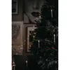 A Christmas tree decorated with candle-shaped lights and berries, with framed artwork on the wall behind it. Podgląd zdjęcia produktu