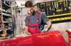 A man in a workshop is working on a red car part. Voir les images du produit