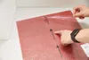 A person's hands are shown peeling protective plastic film from a red carpet tile. Produktbild-Vorschau