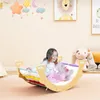 A young girl is playing on a wooden rocking toy in a child's room. Produktbild-Vorschau