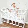 A baby is standing in a crib with bedding. Produktbild-Vorschau