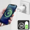 A hand holding a smartphone that is charging, with a power adapter plugged into a wall socket. Náhľad obrázku produktu