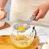 A person is using a stainless steel egg separator to separate an egg yolk from the white over a glass bowl. Produktbild-Vorschau