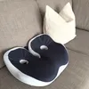 Two cushions are placed on a sofa, one is a dark blue and white ergonomic seat cushion, and the other is a white pillow. Produktbild-Vorschau