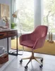 A pink velvet office chair is placed next to a wooden desk in a well-lit room with a large window. Produktbild-Vorschau