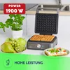 A waffle maker is shown in a kitchen setting with fresh fruit and a plant. Náhľad obrázku produktu