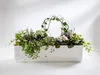 A rectangular white planter filled with various green plants and some small pink and purple flowers, with a decorative wire arch covered in vines in the center. Náhled obrázku produktu