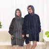 Two people wearing oversized hooded blankets stand in a living room setting. Náhľad obrázku produktu
