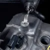 A rotary tool with a burr bit is being used to clean or shape a metal surface, possibly on an engine component. Debris is visible around the area being worked on. Anteprima dell’immagine prodotto
