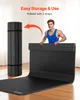 A man is demonstrating how to roll up a black exercise mat for storage. Podgląd zdjęcia produktu