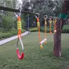 An outdoor obstacle course for children, featuring a slackline with various attachments like swings and climbing grips, set up in a grassy area with trees. Náhľad obrázku produktu