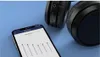A smartphone displaying an equalizer app is placed next to a pair of black over-ear headphones on a blue surface. Voir les images du produit