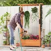 A woman waters plants in a wooden raised garden bed with a trellis structure. Podgląd zdjęcia produktu