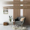 A cozy living room scene featuring a gray armchair, a small side table with a plant and picture frame, a woven basket, and a fluffy rug, with wooden slatted wall panels in the background. Produktbild-Vorschau
