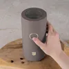 A hand is pressing the button on a taupe electric coffee grinder, which is placed on a wooden surface with coffee beans scattered around. Náhľad obrázku produktu