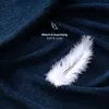 A close-up of a dark blue textured fabric, possibly a blanket or sheet, with a white feather resting on it. Text overlays indicate softness and coziness. Voir les images du produit