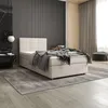 A bedroom scene featuring a beige boxspring bed with a grey blanket and pillows, set against a dark slatted wall and a light wood alcove with curtains. Voir les images du produit