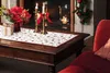 A festive Christmas scene with a coffee table adorned with a runner, candles, flowers, and a gift, next to a fireplace and a red chaise lounge. Náhľad obrázku produktu