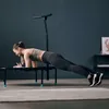A woman is doing a plank exercise on a mini-trampoline in a room. Voir les images du produit