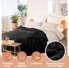 A black blanket is draped over a bed with white bedding, next to a window with plants. Náhled obrázku produktu