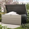 An outdoor storage box filled with cushions, placed on a paved patio with flowering plants and trees in the background. Produktbild-Vorschau