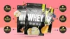 Three bags of whey protein are displayed against a pink gradient background, with various fruits and descriptive icons surrounding them. Produktbild-Vorschau
