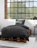 A bed with dark gray bedding is set up on wooden pallets in front of a large window with a view of trees. Produktbild-Vorschau