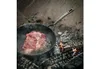 A raw steak is being seared in a cast iron pan over an open fire. Produktbild-Vorschau