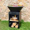 A grill-fire pit with food cooking on top, set up in a grassy area with a stone wall in the background. Anteprima dell’immagine prodotto