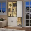 A modern white vitrine with glass doors and LED lighting, showcasing decorative items and books, placed in a living room setting next to a window. Anteprima dell’immagine prodotto