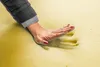 A hand pressing into a yellow foam mattress, showing its softness and support. Produktbild-Vorschau