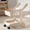 A wooden toy shopping cart is shown on a rug in a room. Produktbild-Vorschau