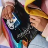A person is taking a small blue Canon camera out of a colorful, rainbow-patterned bag. Anteprima dell’immagine prodotto