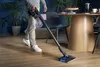A person is vacuuming a wooden floor in a living room. Voir les images du produit